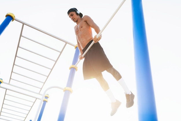 Hombre musculoso haciendo ejercicios de dominadas en la barra horizontal al aire libre Corredor atlético entrenando duro en un día soleado afuera en el bar Deportista haciendo ejercicio en la barra transversal contra el cielo