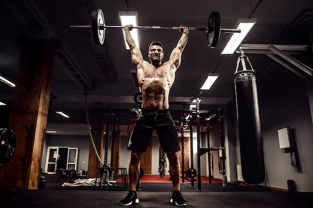 Hombre musculoso haciendo peso muerto una barra sobre su cabeza en el moderno gimnasio