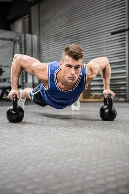 Hombre musculoso haciendo push up con kettlebells en el gimnasio de crossfit