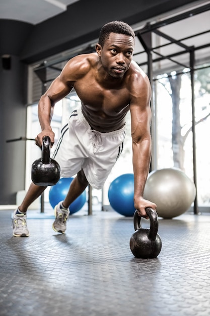 Hombre musculoso haciendo push up con kettlebells en el gimnasio de crossfit