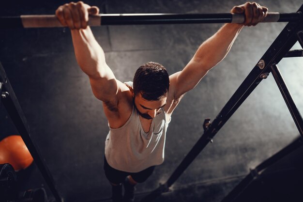 Hombre musculoso joven fuerte haciendo ejercicio pull-up en el gimnasio.