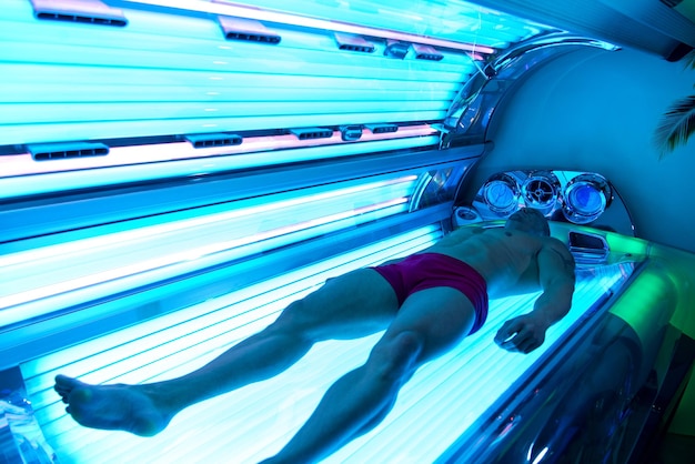 Hombre musculoso joven en solarium en salón de belleza