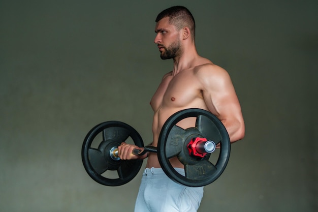 Hombre musculoso levantando pesas en el gimnasio chico guapo se prepara para hacer ejercicios con mancuernas