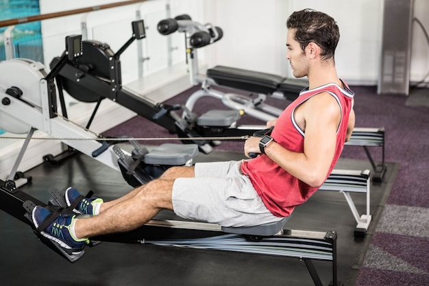 Hombre musculoso en la máquina de remo en el gimnasio