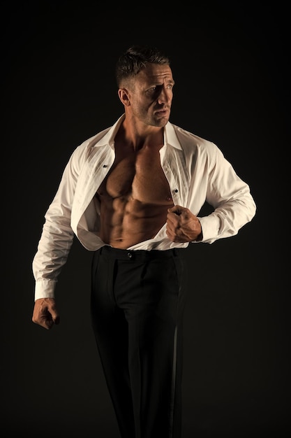 Hombre musculoso mostrar torso en forma con abdominales de seis paquetes en camisa abierta estilo formal fondo negro paquete de seis