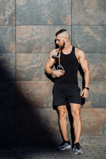 Hombre musculoso o entrenador de fitness con goma de gimnasia estirada posando contra la pared de hormigón