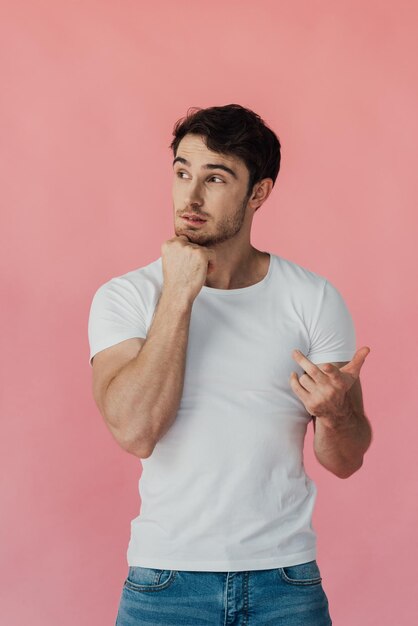 Foto hombre musculoso pensativo en camiseta blanca apoyando la cara con el puño y contando con los dedos aislados en