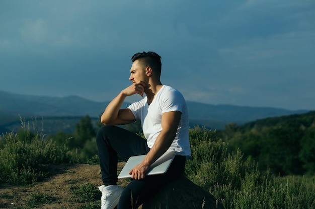 Hombre musculoso pensativo con laptop al aire libre