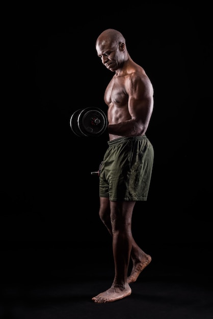 Hombre musculoso de pie haciendo ejercicio para bíceps con mancuernas sobre un fondo negro