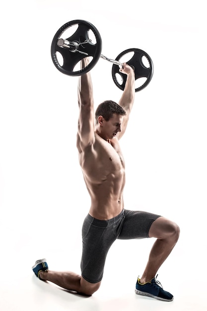 Foto hombre musculoso de pie sobre la rodilla, sosteniendo la barra sobre su cabeza