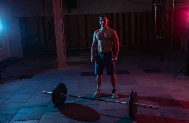 Hombre musculoso poderoso y barra con luz de neón rojoazul en un gimnasio de entrenamiento cruzado