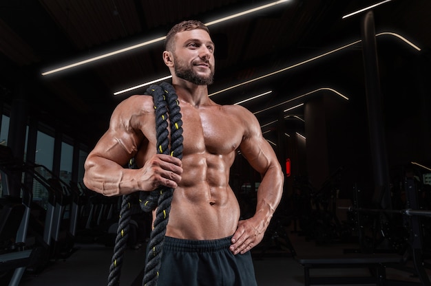 Hombre musculoso posando en el gimnasio con una cuerda. Concepto de fitness.