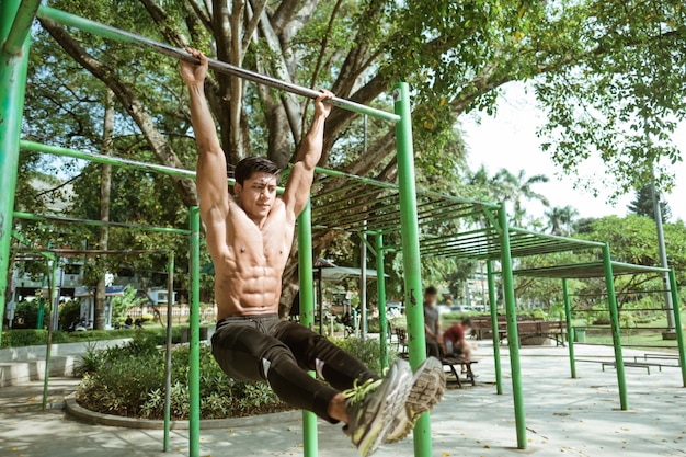 Un hombre musculoso sin ropa haciendo L ejercicios de pull-up con barra de hierro en el parque