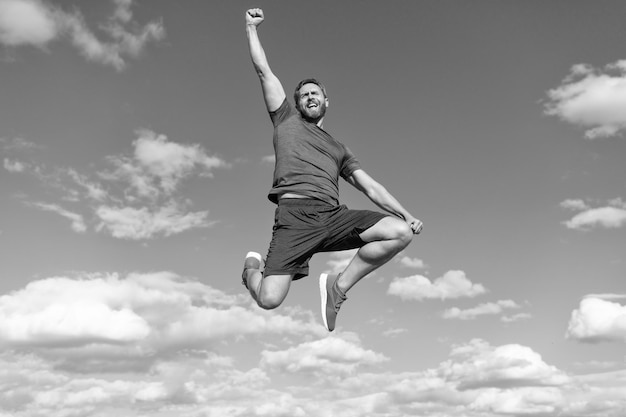 Hombre musculoso saltando en ropa deportiva al aire libre en el éxito de fondo del cielo