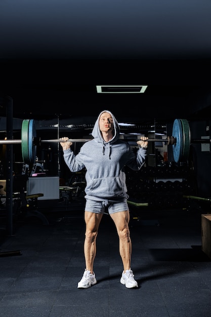 Hombre musculoso sentadillas con barra en el gimnasio