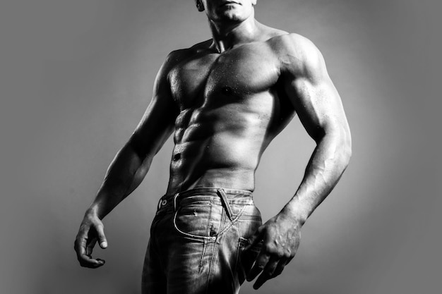 Hombre musculoso sexy fuerte en jeans sobre fondo gris aislado cuerpo en forma ideal