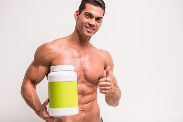 Hombre musculoso sonriente con el tarro de proteína.