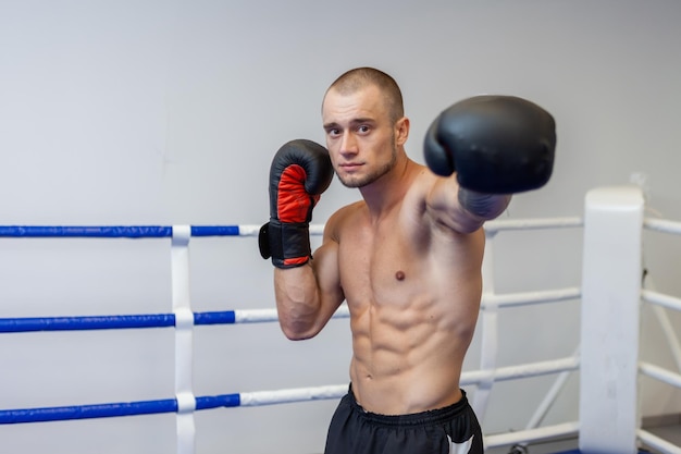 Hombre musculoso con el torso desnudo entrena puñetazo con guantes de boxeo en el ring