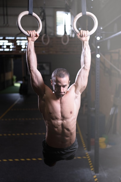 Hombre musculoso trabajando en anillos de gimnasia en un gimnasio de entrenamiento cruzado