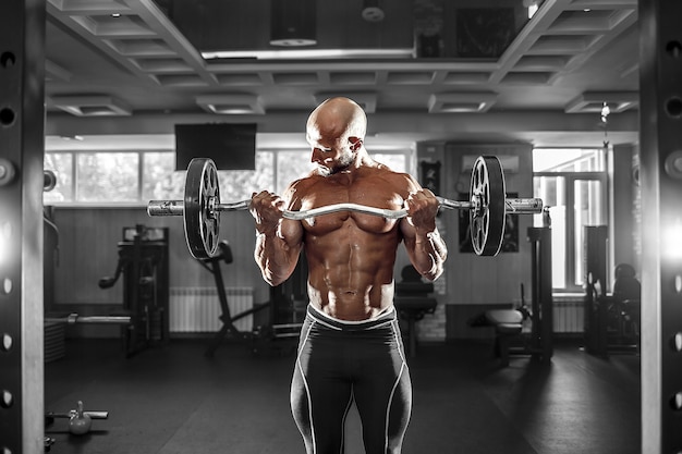 Hombre musculoso trabajando en el gimnasio haciendo ejercicios con pesas
