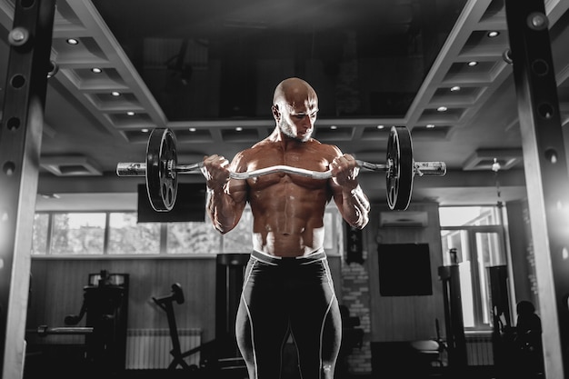 Hombre musculoso trabajando en el gimnasio haciendo ejercicios con pesas