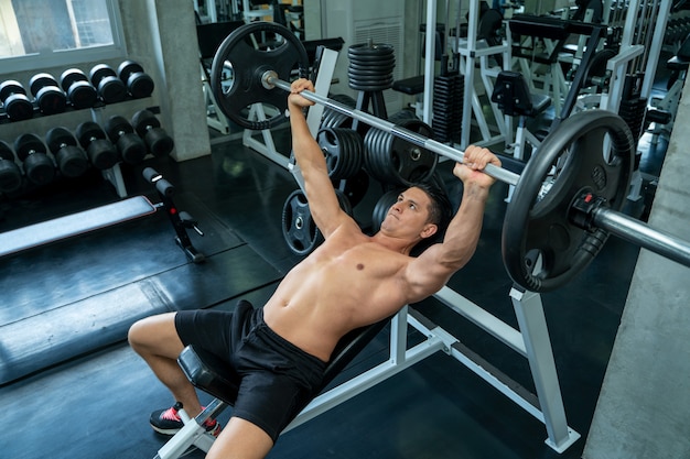 Hombre musculoso trabajando con placa de barra para hacer ejercicio en el  gimnasio.