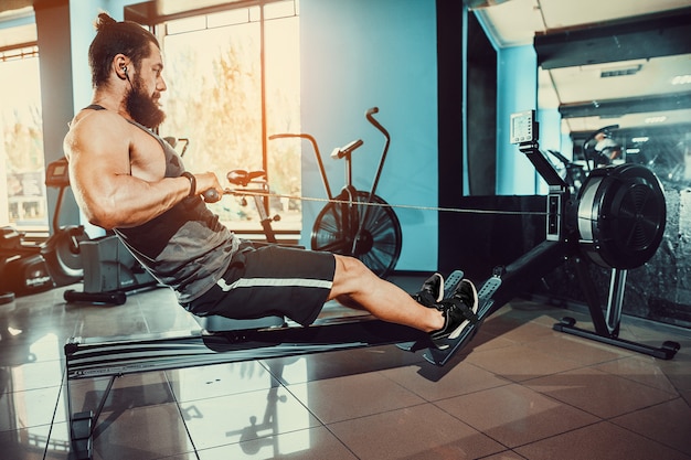 Hombre musculoso usando la máquina de remo en el gimnasio