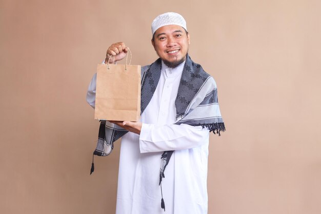 Foto hombre musulmán adicto a las compras asiático sonriendo mientras sostiene una bolsa de compras en fondo beige