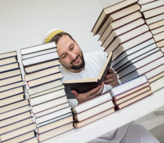 Hombre musulmán adulto en la biblioteca leyendo libros