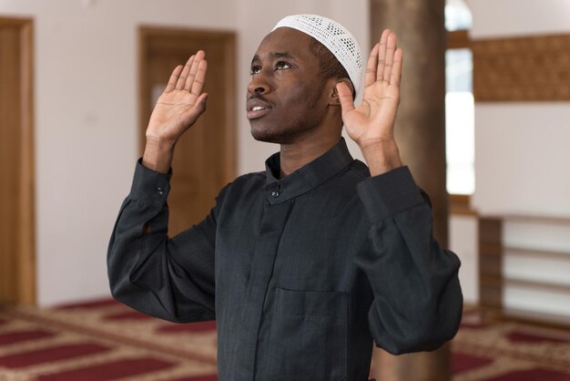 Hombre musulmán africano haciendo oración tradicional a Dios mientras usa una gorra tradicional Dishdasha