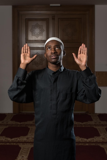 Hombre musulmán africano haciendo oración tradicional a Dios mientras usa una gorra tradicional Dishdasha