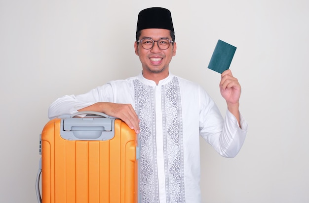 Hombre musulmán asiático con equipaje sonriendo feliz y una mano mostrando el pasaporte