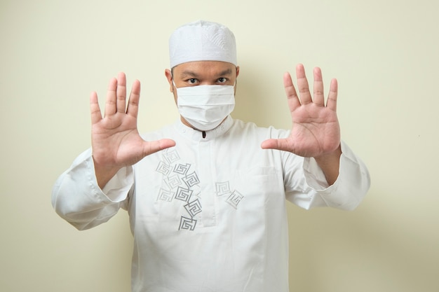 Un hombre musulmán asiático gordo que lleva una máscara con la mano que simboliza el gesto de la parada