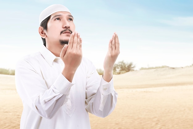 Hombre musulmán asiático de pie mientras levanta las manos y reza con un fondo de cielo azul