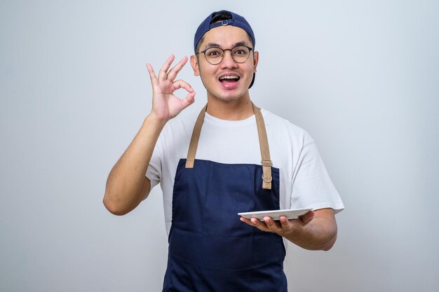 Hombre musulmán asiático que muestra una expresión emocionada mientras sostiene un plato vacío