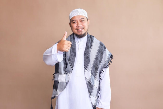 Hombre musulmán asiático sintiéndose orgulloso despreocupado confiado y feliz sonriendo positivamente con los pulgares hacia arriba