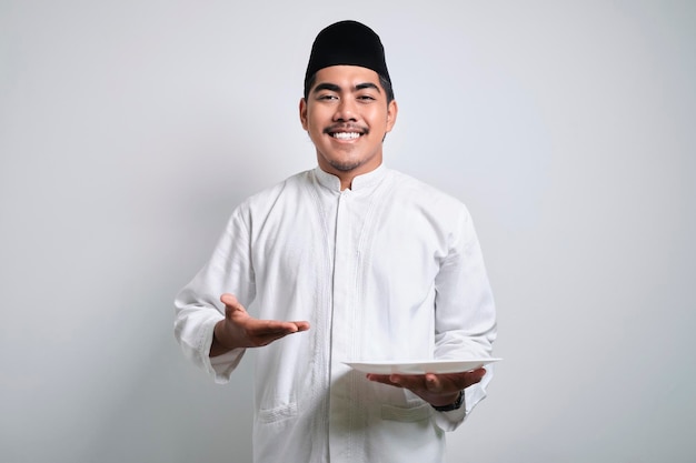 Hombre musulmán asiático sonriente mirando a la cámara presentando algo en un plato vacío