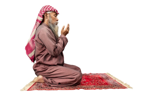 Hombre musulmán con barba usando keffiyeh con agal en posición de oración salat en la alfombra de oración