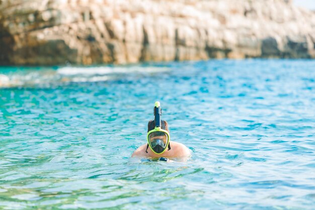 Hombre nadando con máscara de buceo en agua de mar azul celeste