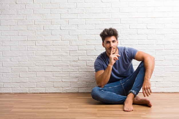 El hombre natural joven se sienta en un piso de madera guardando un secreto o pidiendo silencio, cara seria, concepto de la obediencia