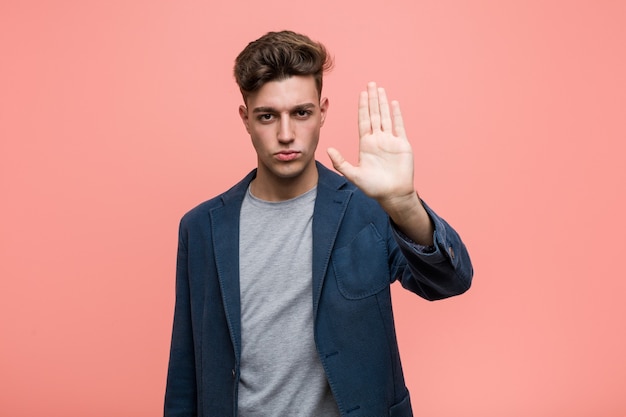 Hombre natural de negocios joven de pie con la mano extendida mostrando la señal de stop, impidiéndote.