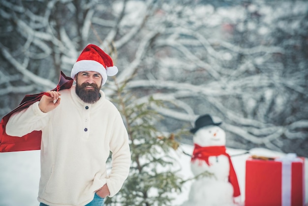 Hombre de Navidad y muñeco de nieve sobre fondo blanco como la nieve. Muñeco de nieve y divertido hombre barbudo en la nieve. Hipster Santa Claus. Vacaciones de navidad y año nuevo.