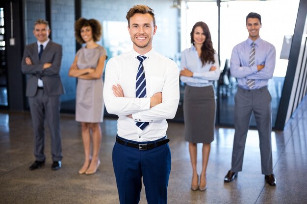 Hombre de negocios acertado que sonríe mientras que sus colegas que se colocan detrás de él en oficina