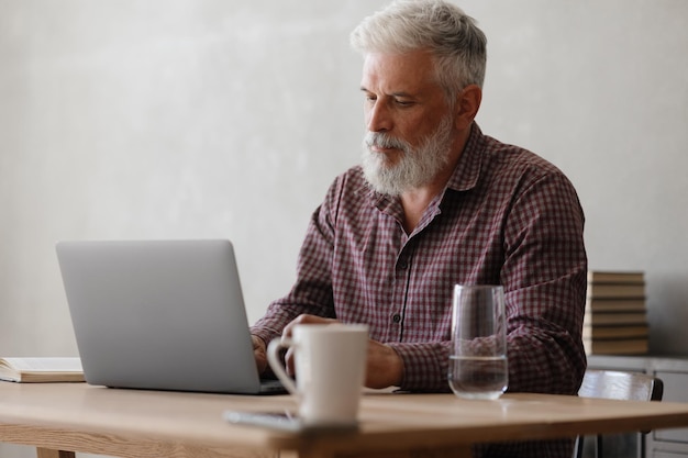 Hombre de negocios adulto con canas está trabajando en una computadora portátil en su oficina de finanzas y marketing de carrera