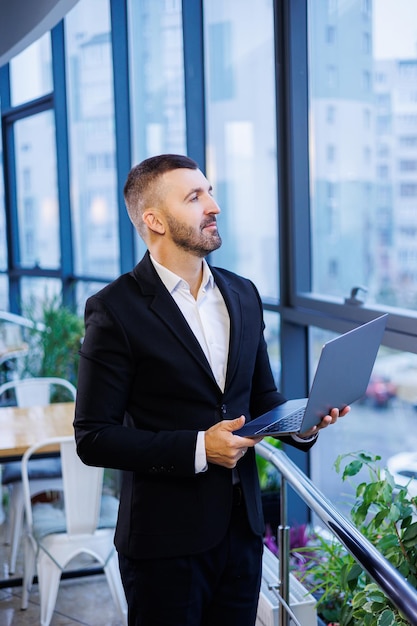 Hombre de negocios adulto, maestro, mentor mira por la ventana grande de su oficina. Trabaja en la oficina. Desarrollo de un nuevo proyecto empresarial.