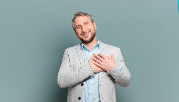 Hombre de negocios adulto que se siente romántico, feliz y enamorado, sonriendo alegremente y tomados de la mano cerca del corazón