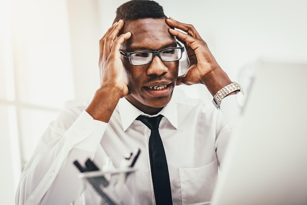Un hombre de negocios africano ansioso se sienta en la oficina y sostiene su cabeza con las manos.