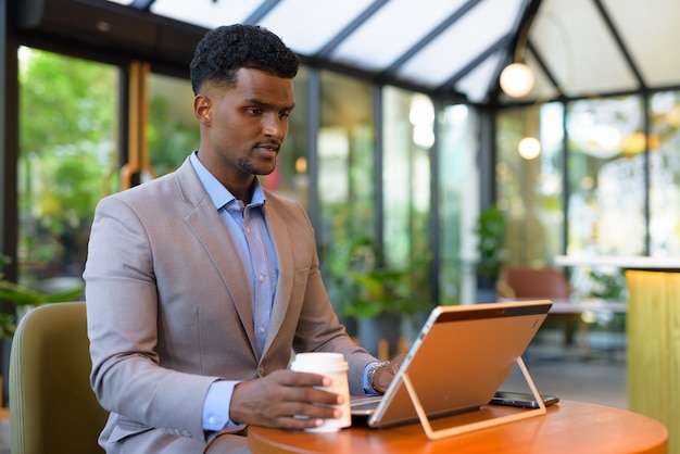 Hombre de negocios africano en la cafetería trabajando con ordenador portátil