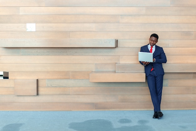 Hombre de negocios africano elegante que usa el ordenador portátil en oficina con el copyspace