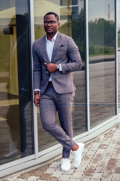 Hombre de negocios africano de moda y exitoso hombre guapo americano en un elegante traje de lujo posando en el modelo de moda de fondo de rascacielos de oficina de centro de negocios de la calle